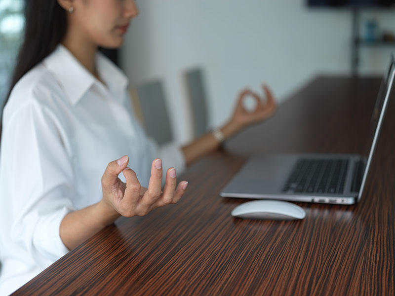 a woman sitting at a desk with a laptop with her hands in a meditation position