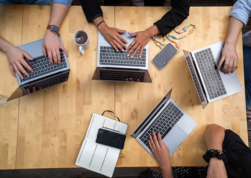 view from overhead of a team of web developer around a table with laptops and electronic devices